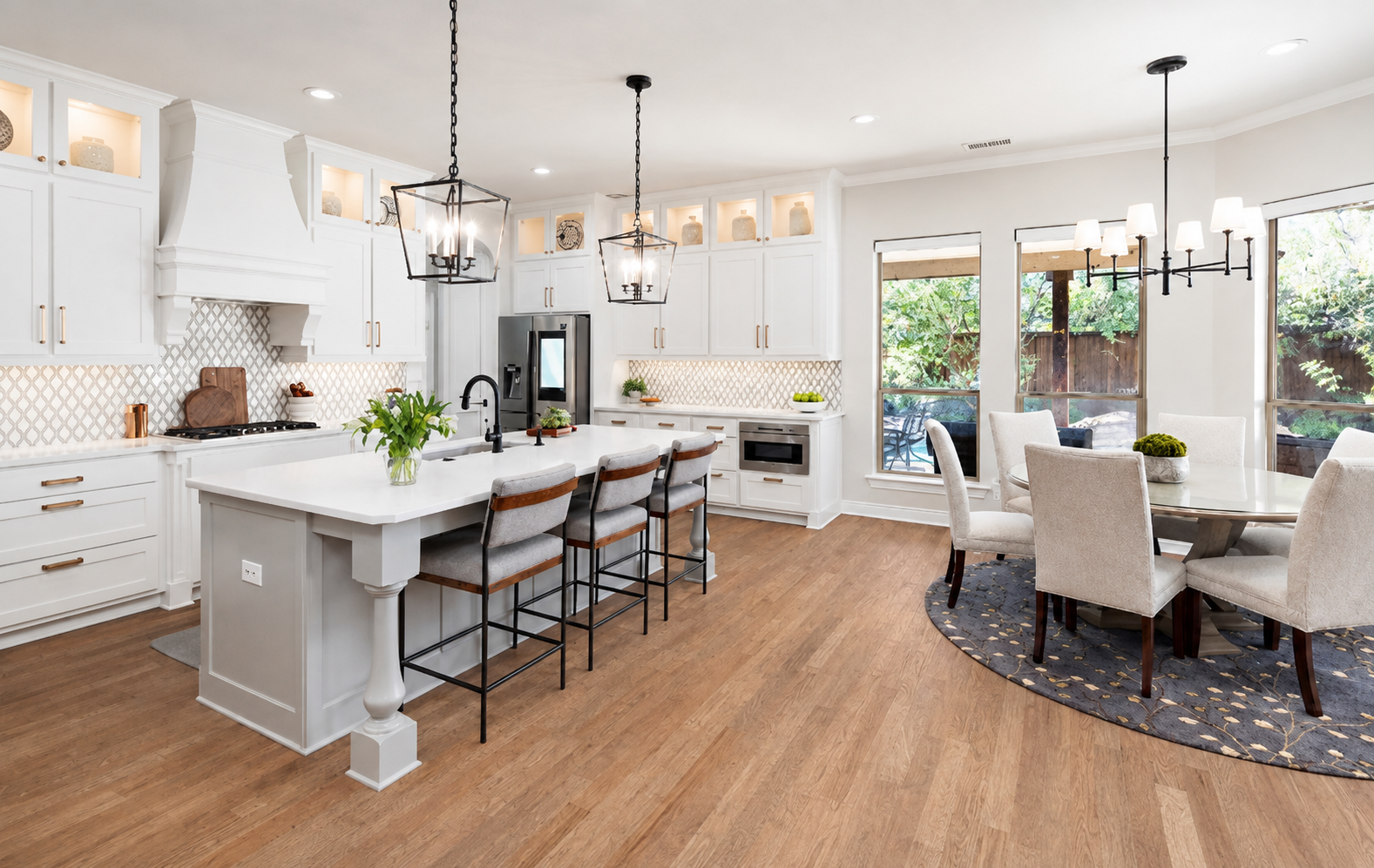 Bright white kitchen and dining area with gray island, lantern pendants, and hardwood floors