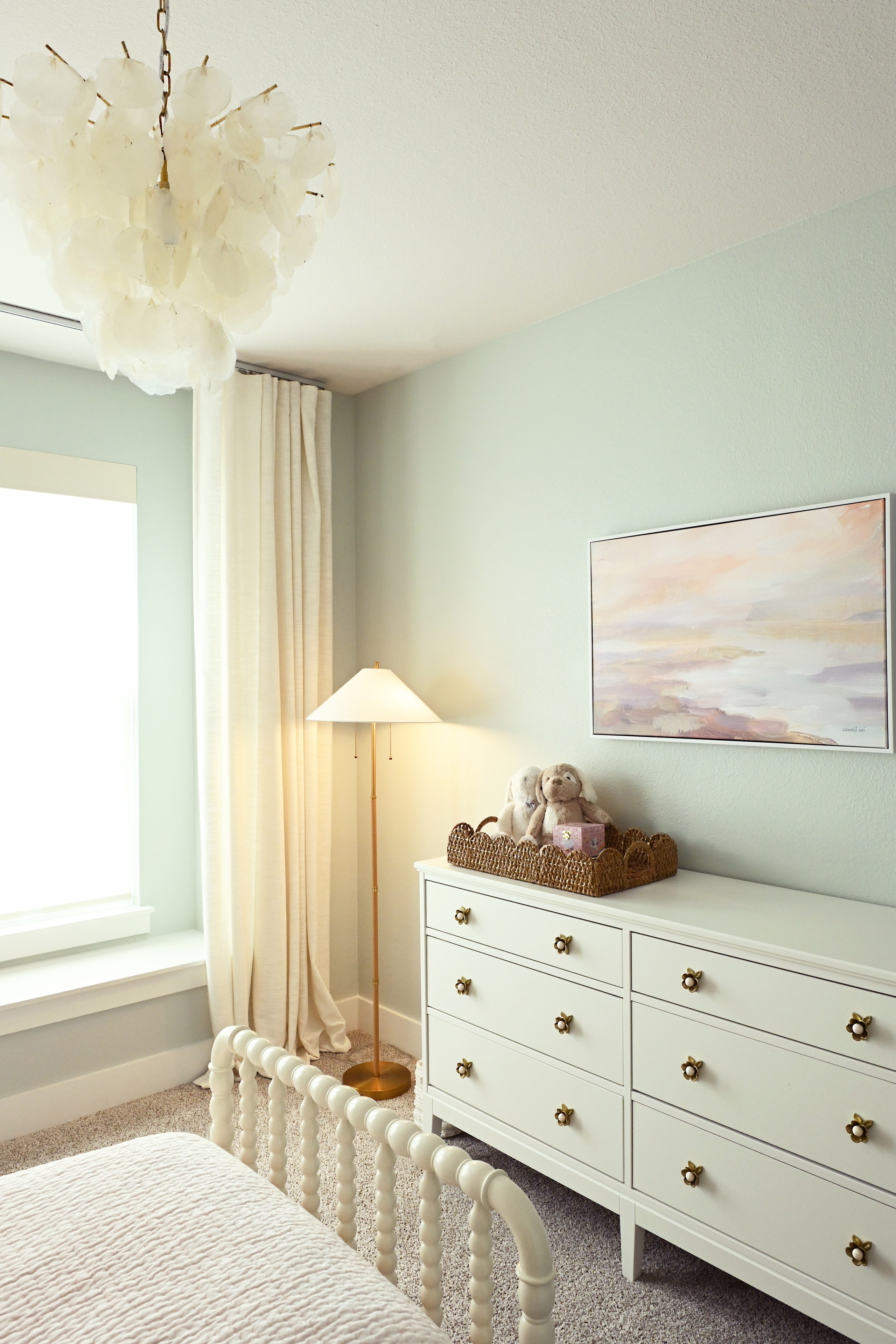 Nursery with mint green walls, white dresser, brass hardware, and capiz chandelier
